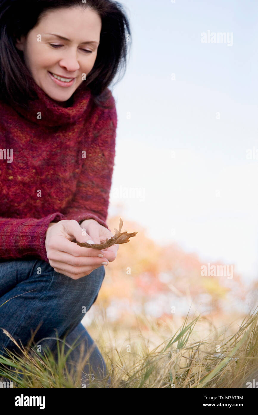 Close-up of a mature woman holding a maple leaf and smiling Stock Photo