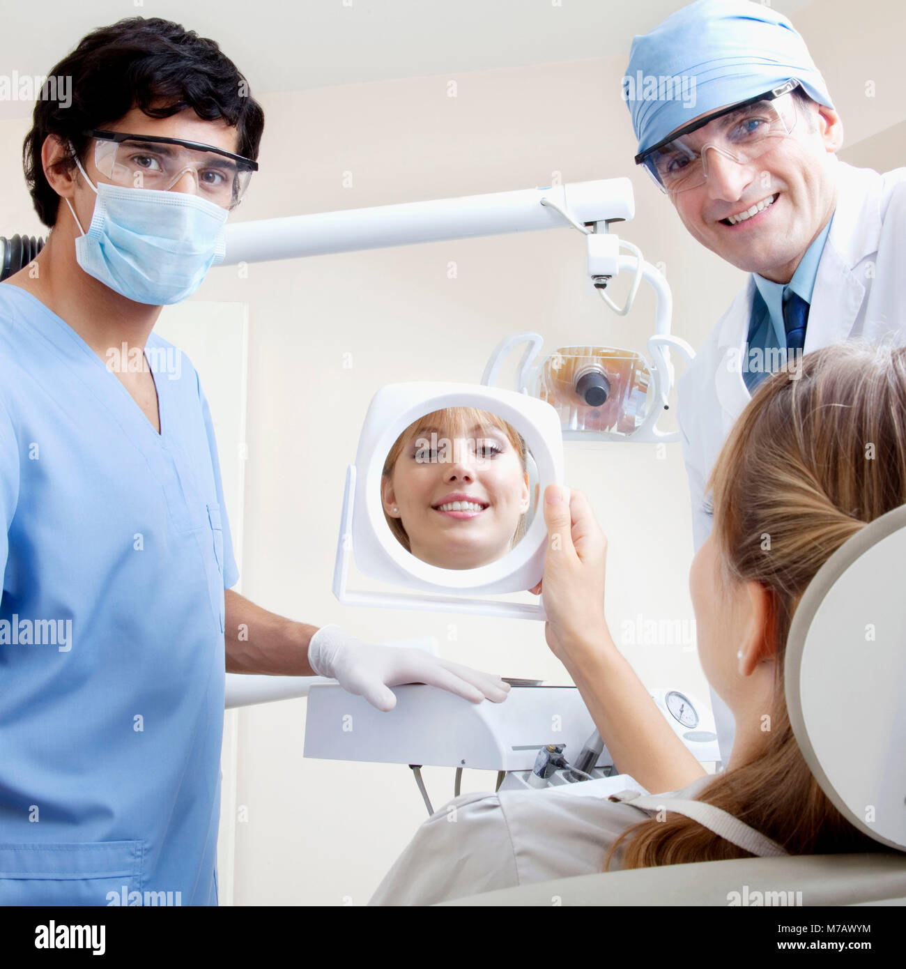 Woman looking in mirror with two male dentists in clinic hires stock