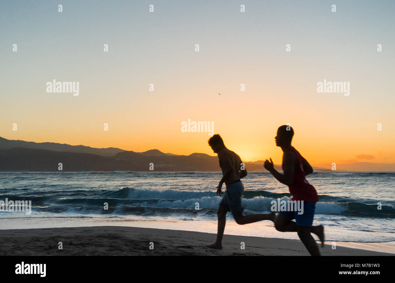 Two young men jogging on beach at sunset Stock Photo