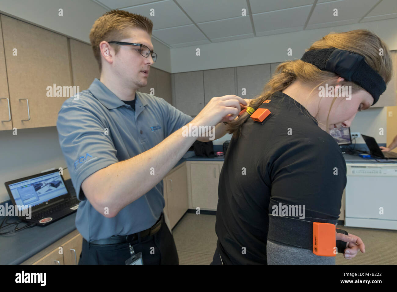 Auburn Hills, Michigan USA - 9 March 2018 - Bradley Roettger adjusts sensors on a motion suit worn by Taylor VanDyke at Fiat Chrysler Automobiles. The sensors translate movements onto a virtual reality computer screen. FCA engineers use the equipment to determine the best methods for assembling cars that are still in the design stage. Credit: Jim West/Alamy Live News Stock Photo