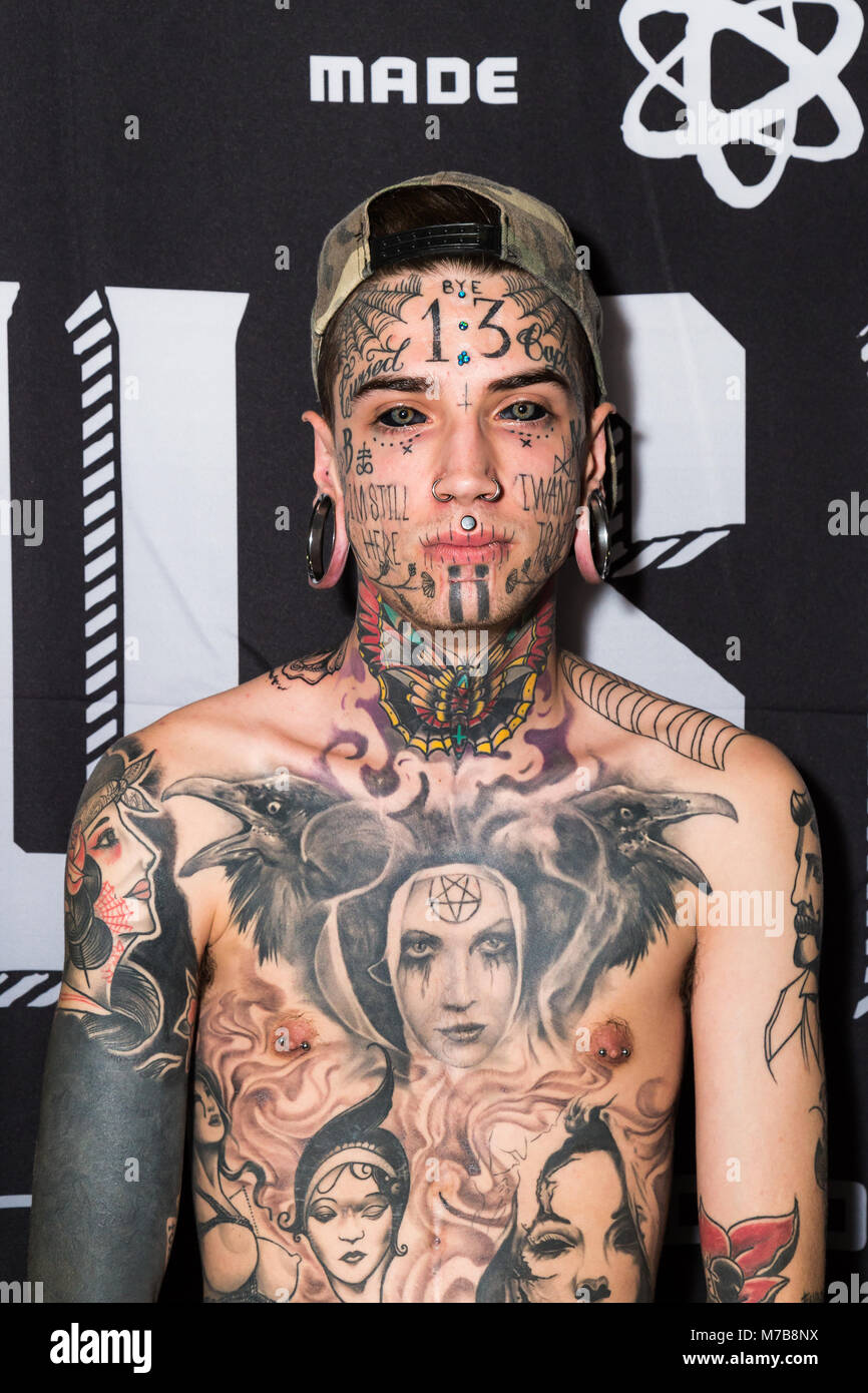 A young man with stretched ear lobes and heavily tattooed chest and face adds to his tattoo collection at the Australian Tattoo Expo, International Convention Centre, Darling Harbour, Sydney. This event represents the culture of body ink and also promotes the skills of world-renowned artists in Australia and around the world. Stock Photo