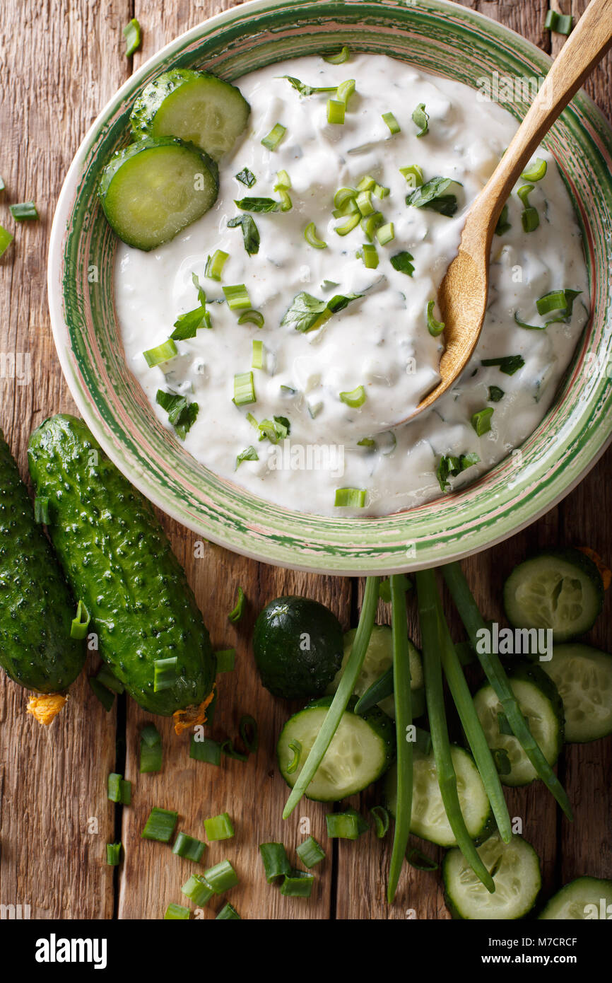 Homemade Indian raita dressing with herbs, spices and cucumber close-up in a bowl on the table. Vertical top view from above Stock Photo
