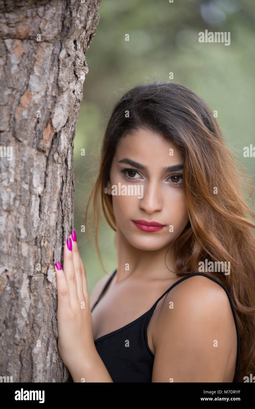 Beautiful young woman hand touching a tree looking away Stock Photo - Alamy