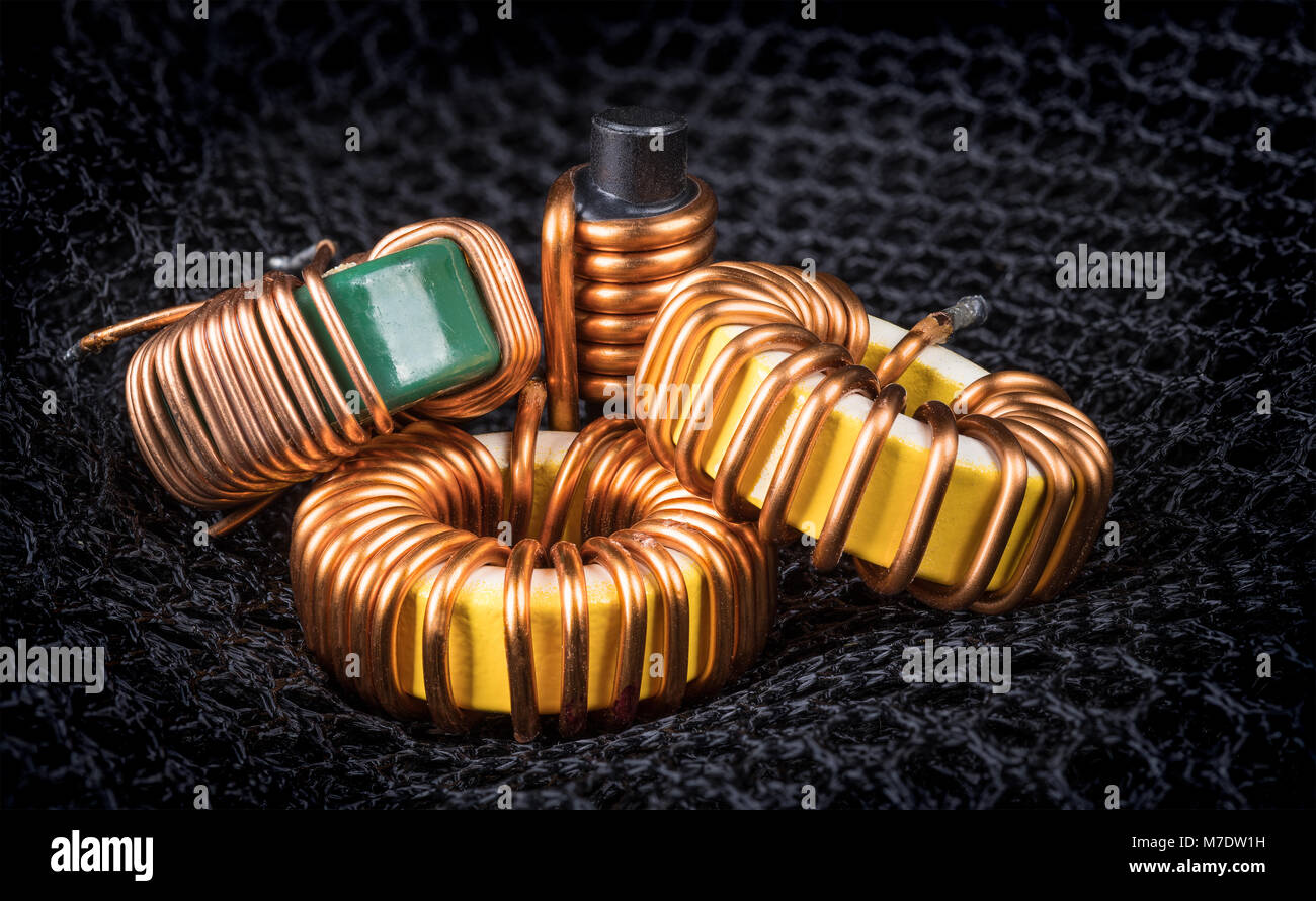 Group of coils with magnetic core and copper winding. Beautiful close-up of toroidal inductors and the solenoid on background from hexagonal mesh. Stock Photo