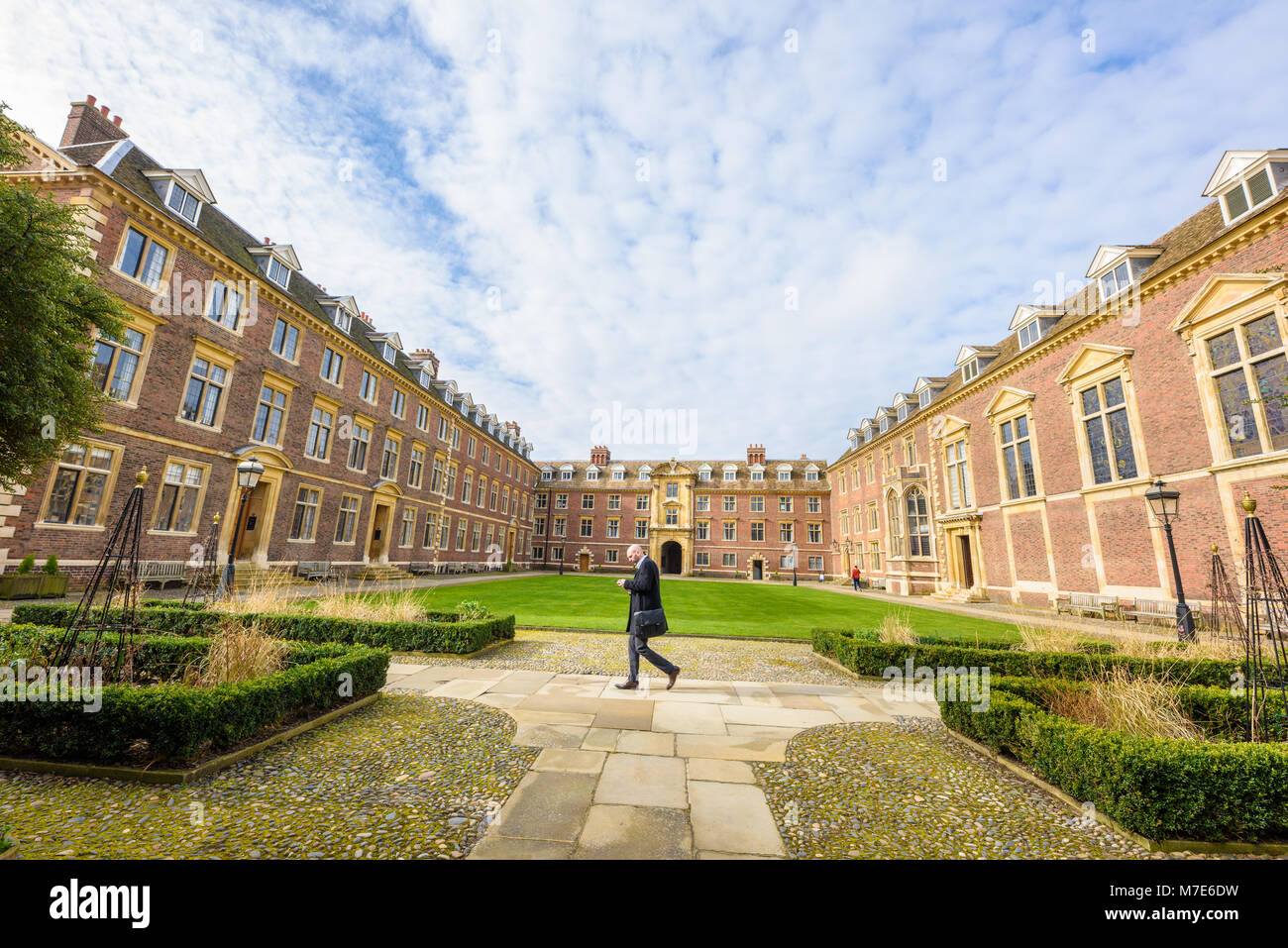 A man, looking a his phone, walks along a path in the main main courtyard at St Catherine's college, university of Cambridge, England. Stock Photo