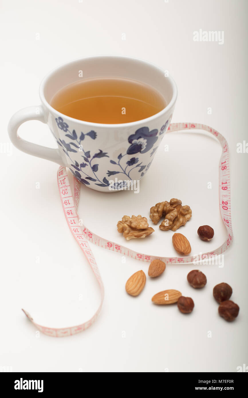 Assorted dried healthy nuts with green tea and a tape measure in a concept of weight loss