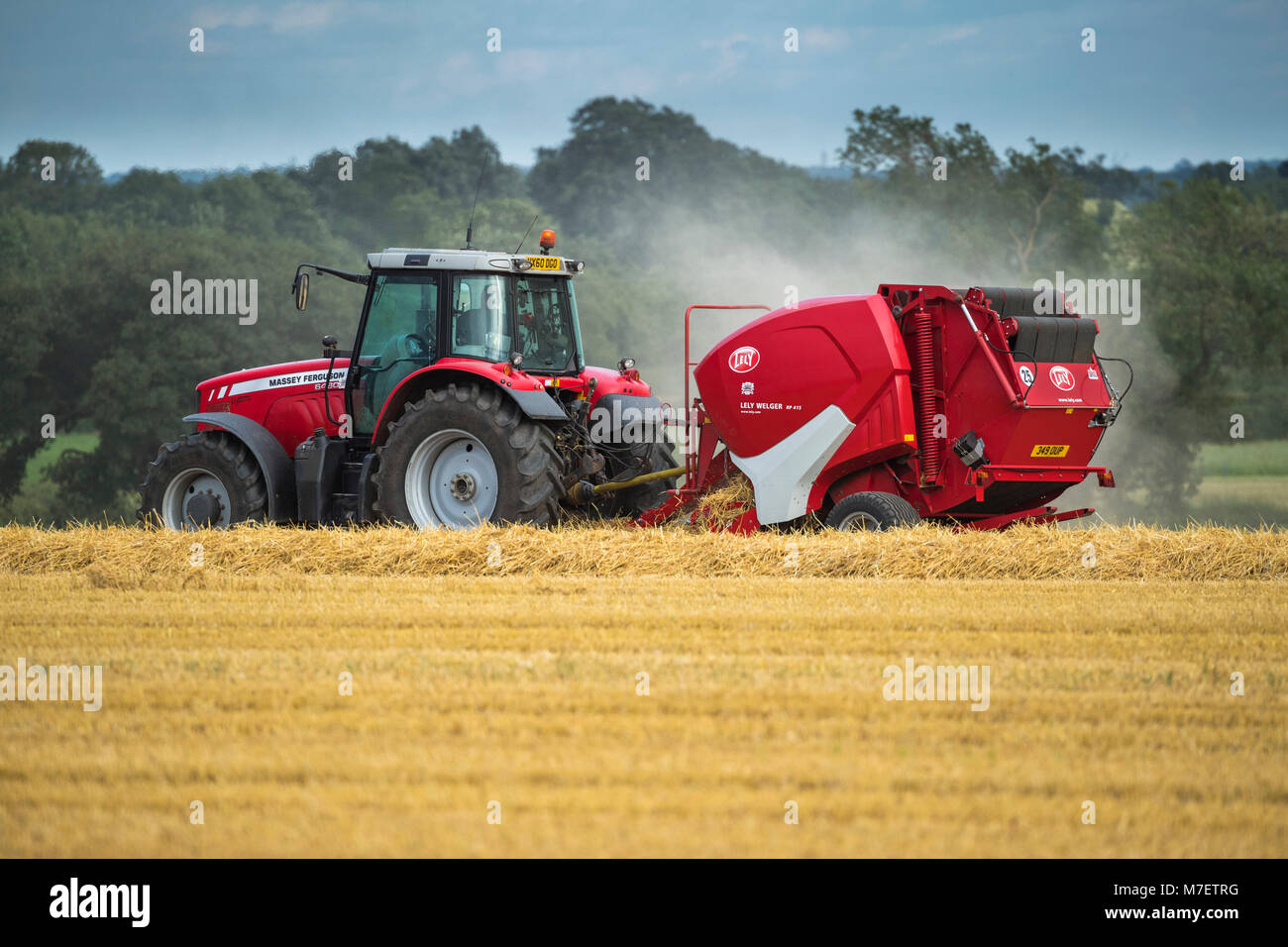 Farmer or man in bright red farm tractor pulling a round baler, is driving & working in a field, baling straw - Whixley, North Yorkshire, England, UK. Stock Photo
