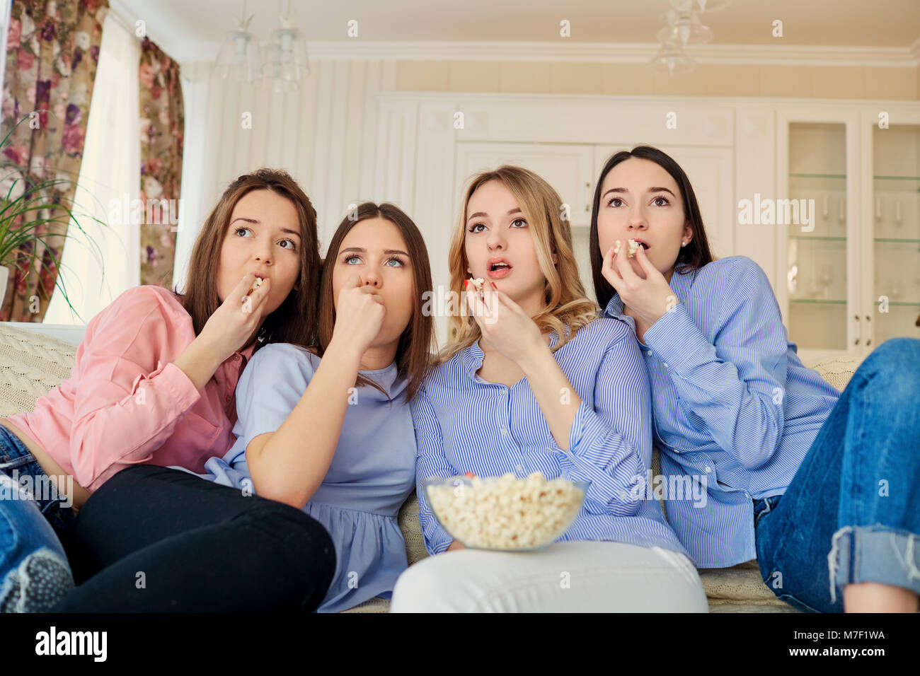 Young girls watching TV, eating popcorn sitting on the couch. Stock Photo