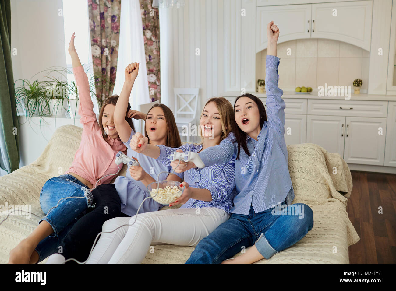 Girlfriends are playing video games sitting on the couch. Stock Photo