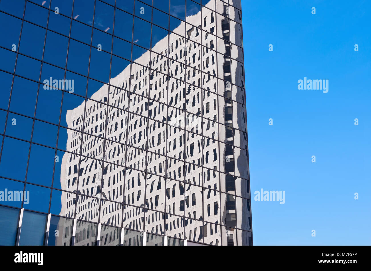 abstract of glass skyscraper with reflections of another skyscraper against blue sky Stock Photo