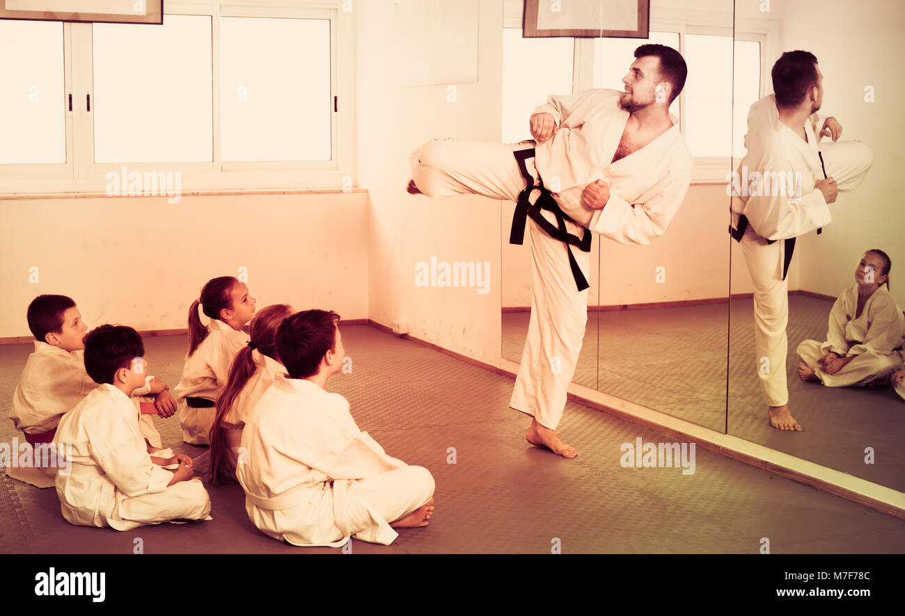 Young positive man training new karate moves with teenagers during class. Focus on girl Stock Photo