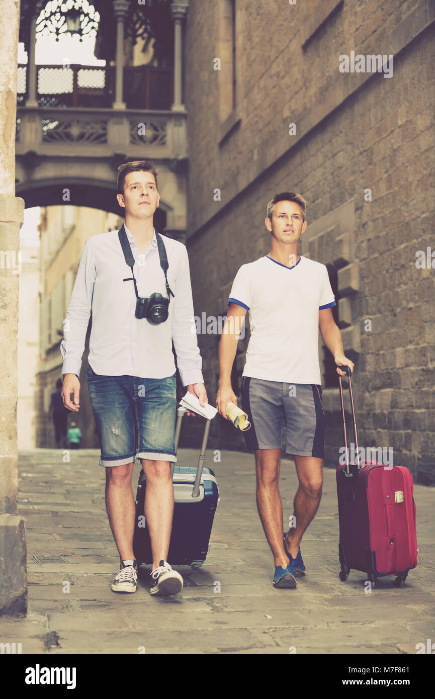positive spanish male couples with travel bags walking the city Stock