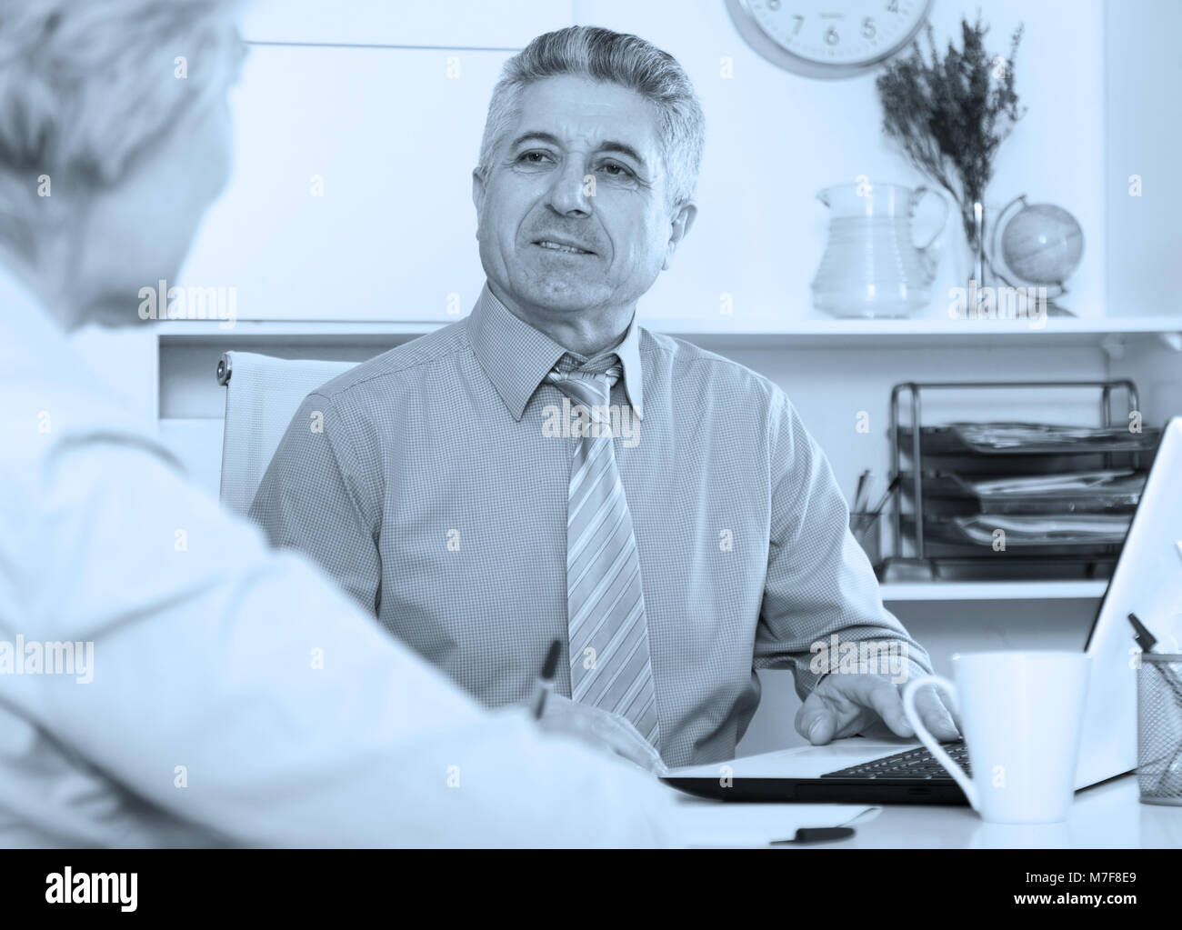 Mature head gives task to assistant at office at table Stock Photo - Alamy