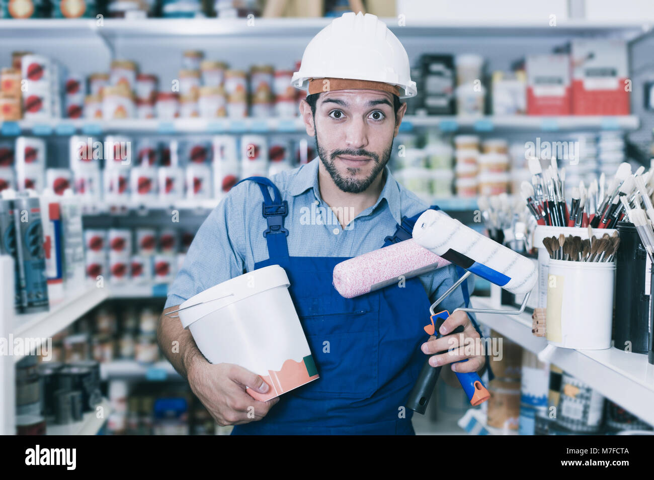 Positive workman in blue overalls with paint and brushes in hands in store Stock Photo Alamy
