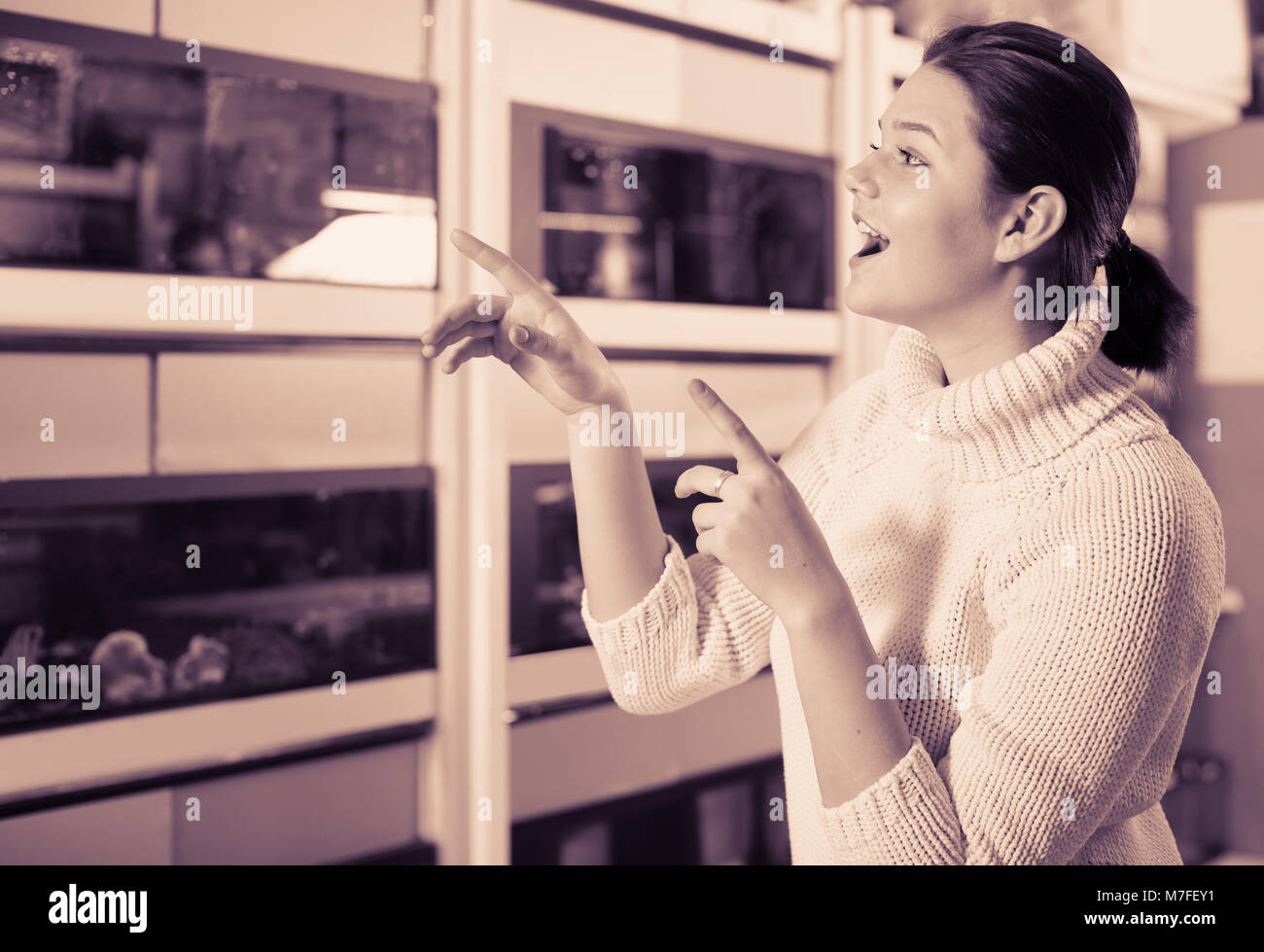 Teenage girl in aquarium shop is looking at different colored fish on several rows of shelves with aquariums. Stock Photo