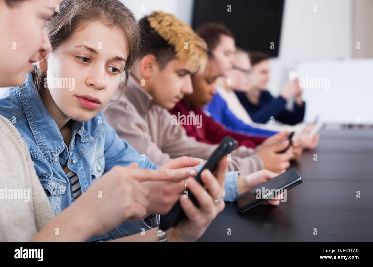 Young male and female students playing with their smartphones in school
