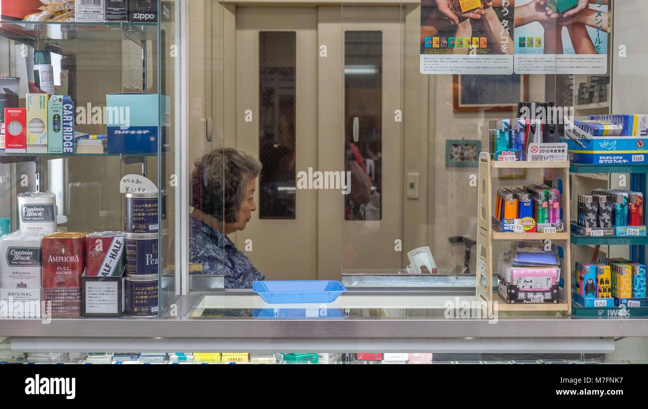 Japanese woman sitting inside  street side tobacco shop with loose tobacco and cigarette packs in window in Kamakura Japan. Stock Photo