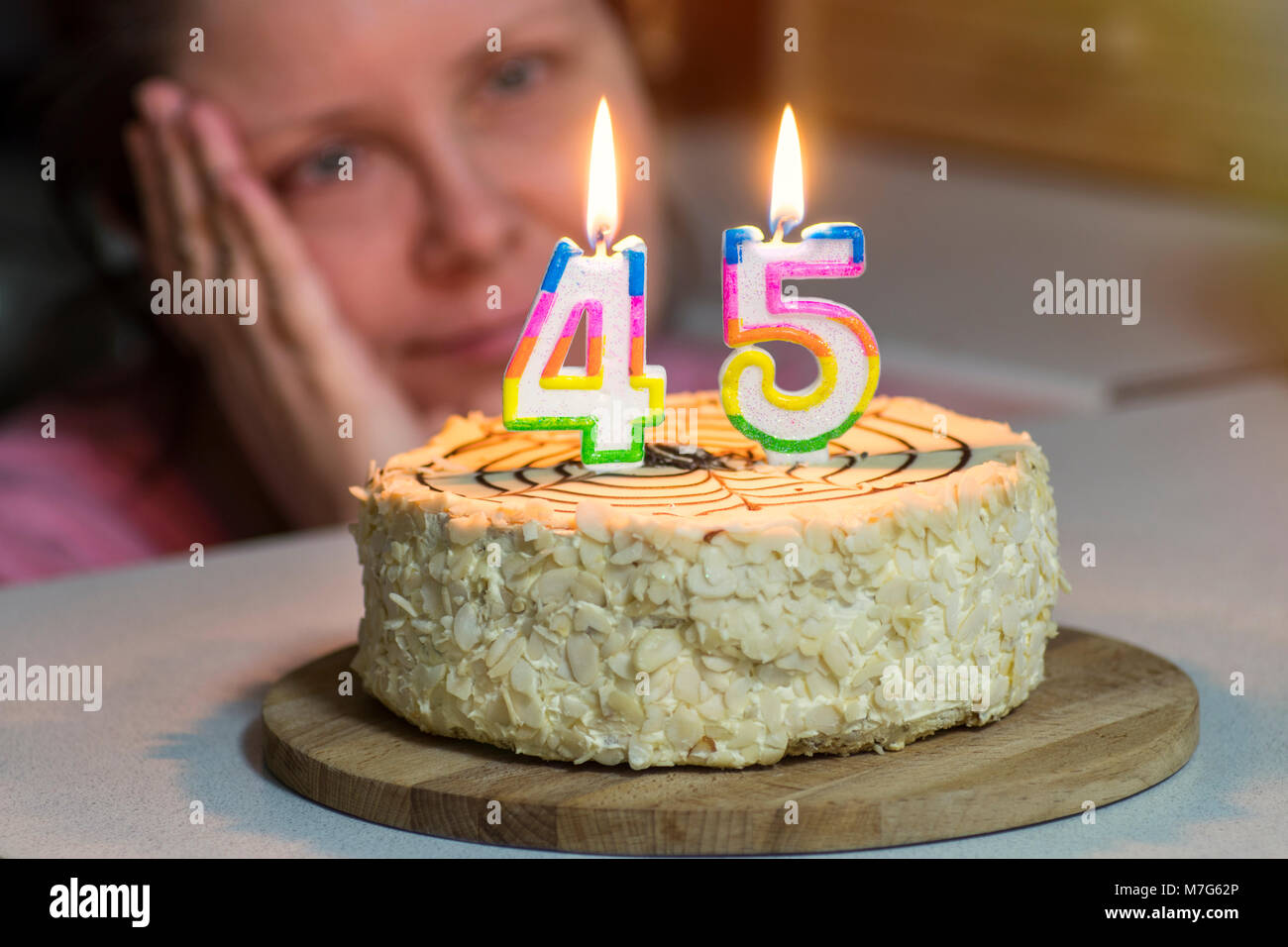 woman is not young looking at cake, candles are burning in the form of