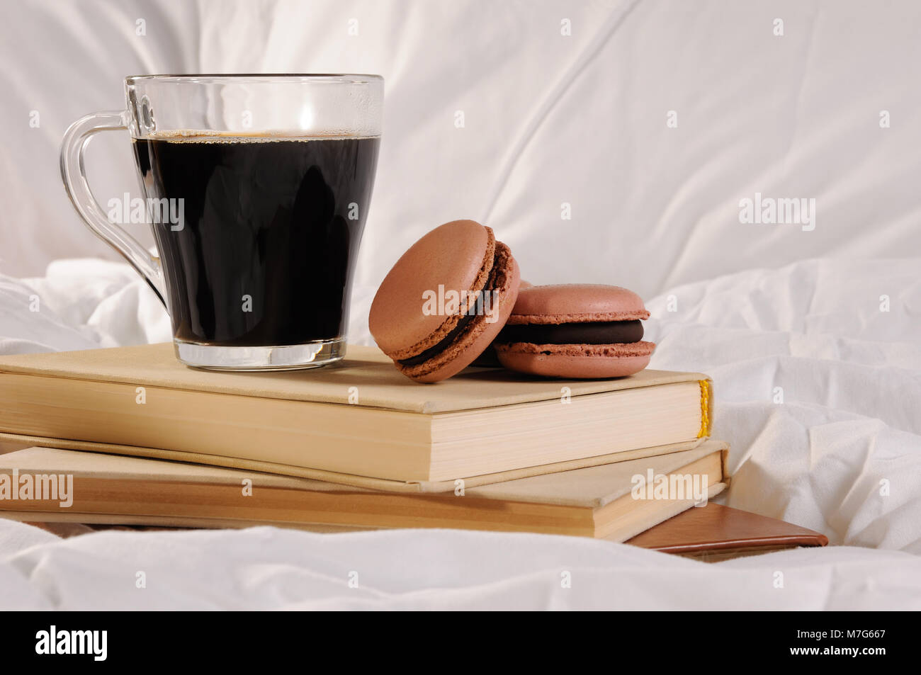 Morning cup of coffee with chocolate cakes Macaroons, on a pile of books in bed. Stock Photo