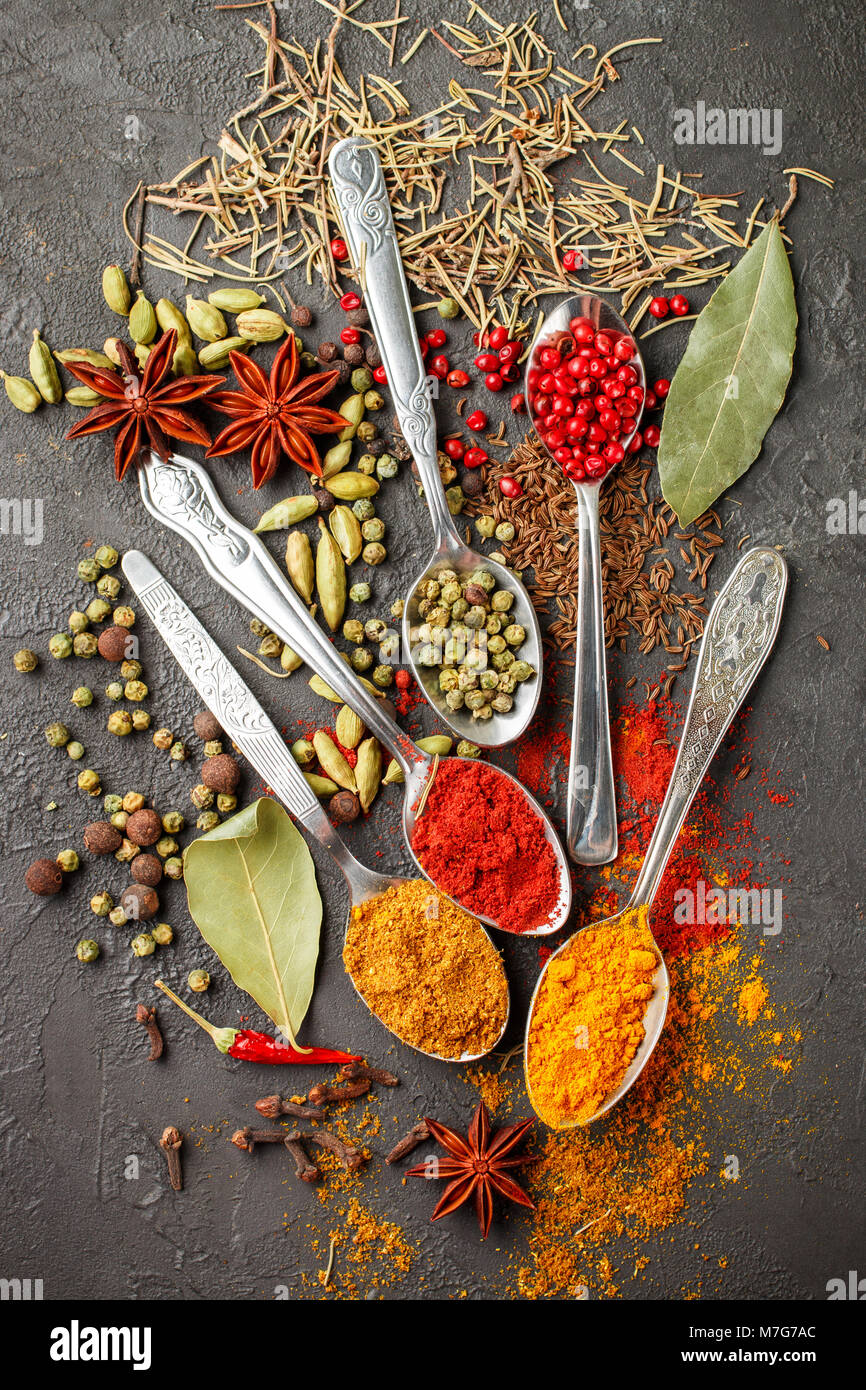 Variety of natural spices, seasonings and herbs in spoons on the stone