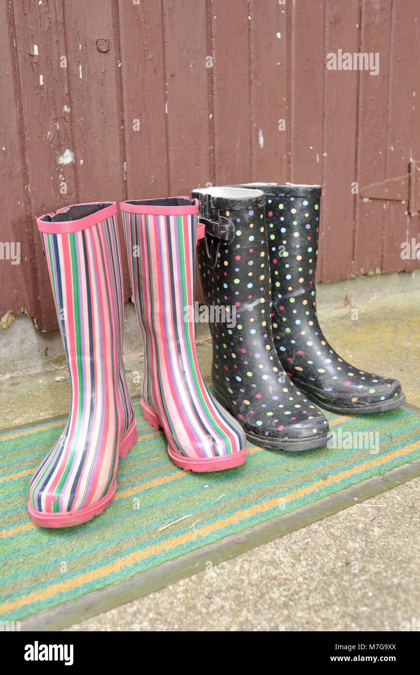 Two pairs of colorful women farmer or gardener boots on a mud mat by the back door Stock Photo