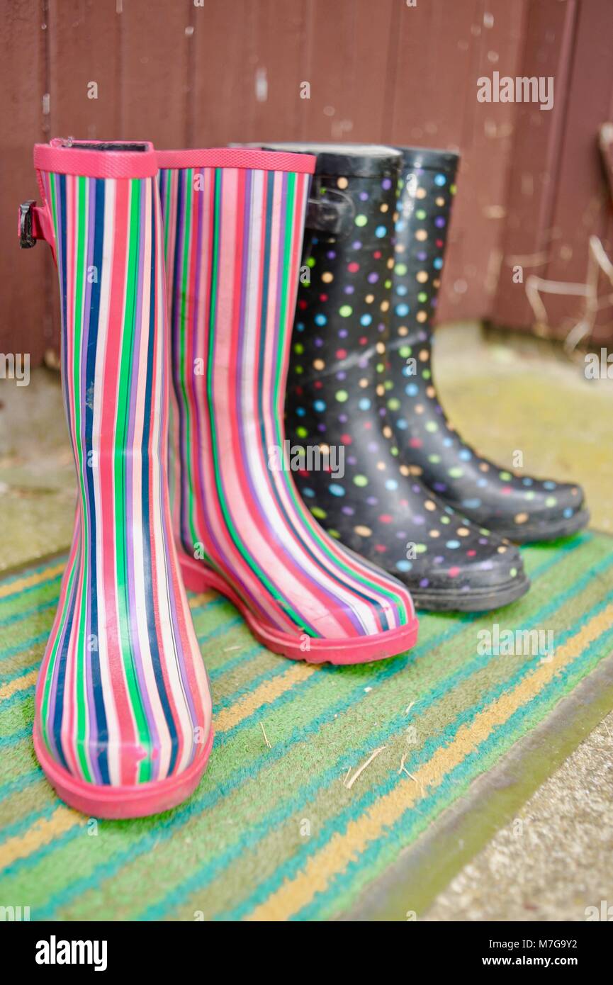 Two pairs of colorful women farmer or gardener boots on a mud mat by the back door Stock Photo