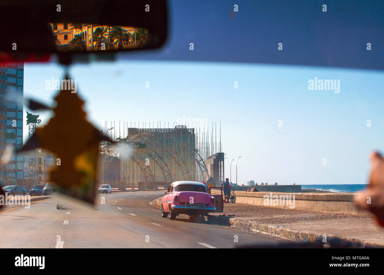 A hot pink classic car is broken down on the Malecón in Havana, Cuba.  The U.S. Embassy is in the far background. Stock Photo
