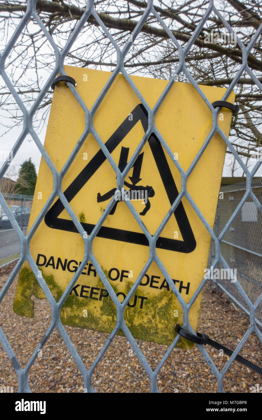 A sign hanging on the mesh fence surrounding an electrical sub station warns of the danger of death by electrocution posed by the electrical equip. Stock Photo