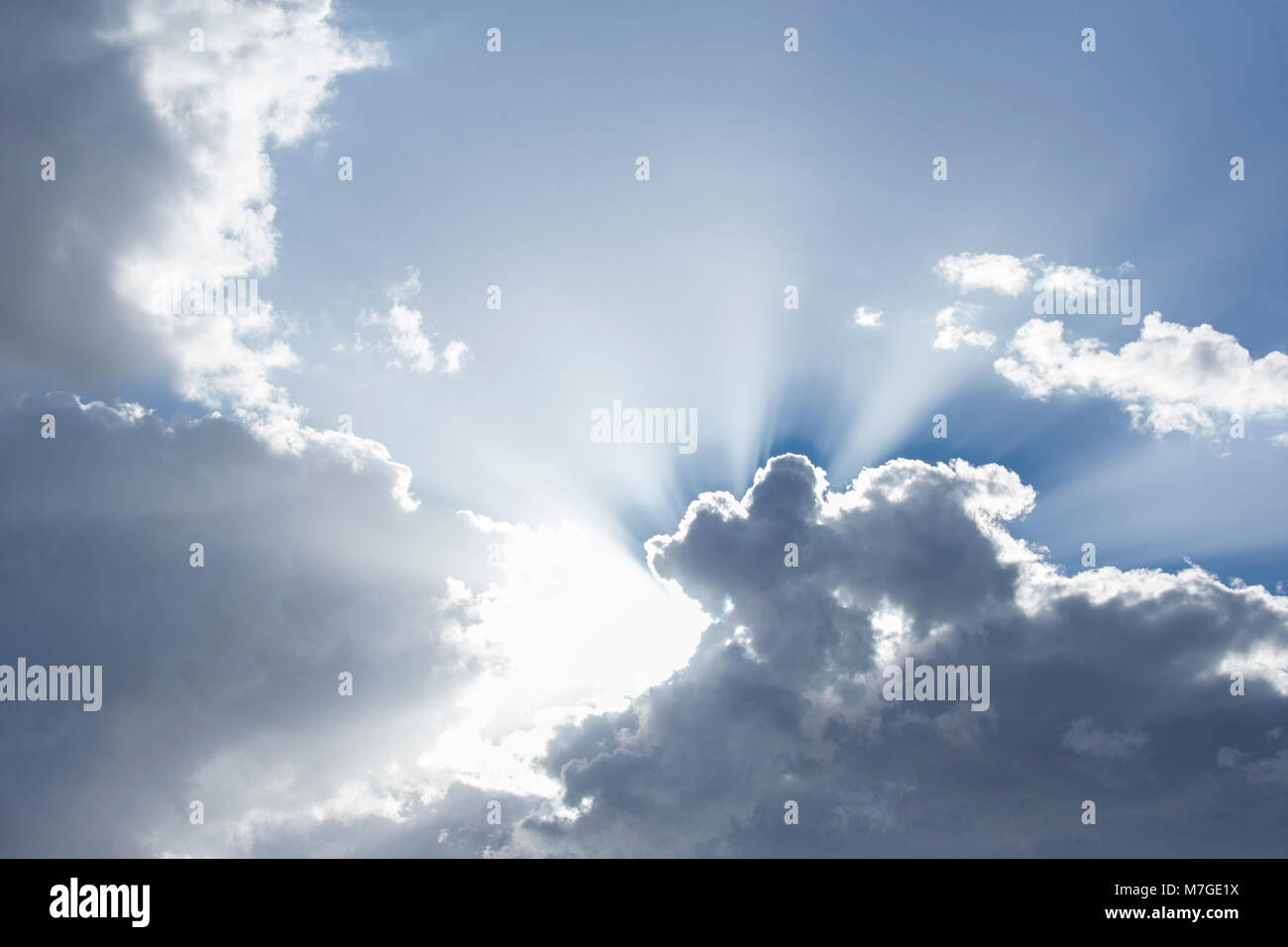 Sun rays coming out from behind clouds in bright blue skyninspiring Stock Photo