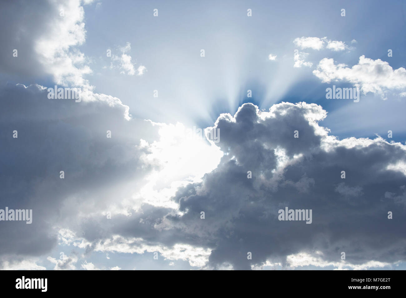 Sun rays coming out from behind clouds in bright blue skyninspiring Stock Photo