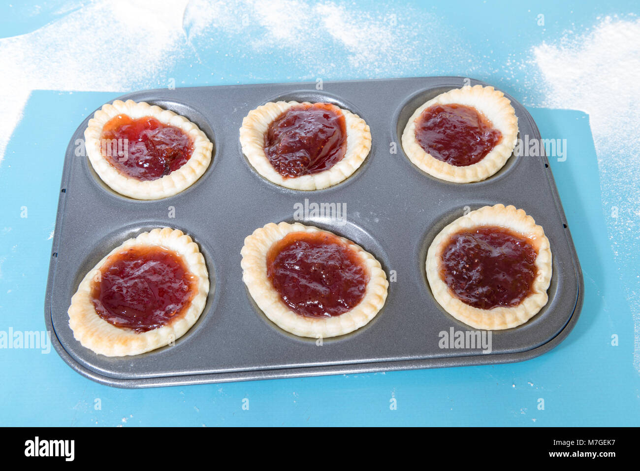 Jam tarts homemade baking tray on a blue formica worktop. Stock Photo