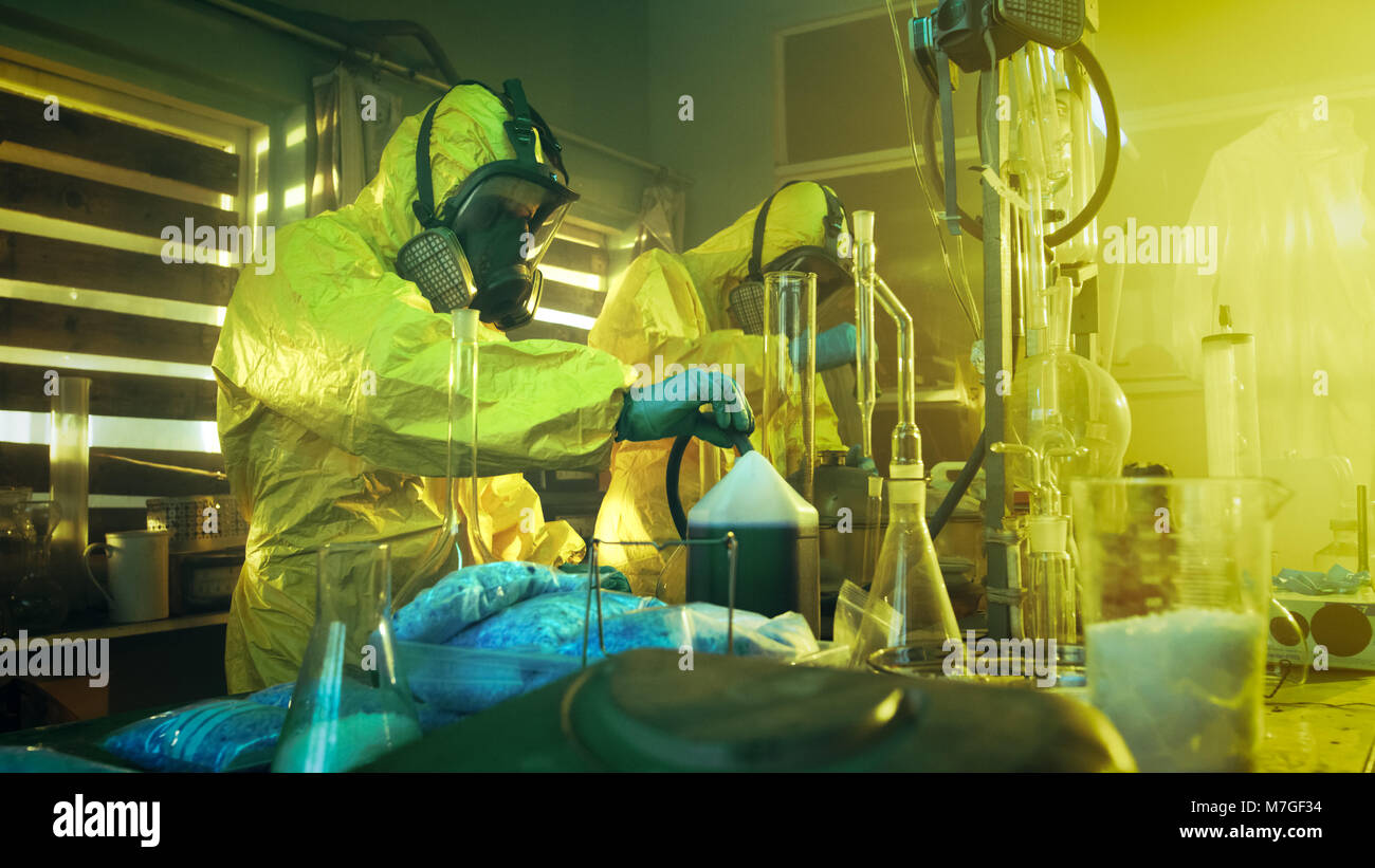 In the Underground Laboratory Two Clandestine Chemists Wearing Protective Coveralls and Masks Cook Drugs. They Work with Beakers, Distillation. Stock Photo