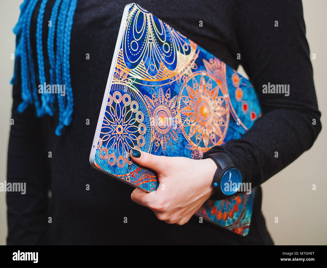 Young woman with long blue braids holding a laptop with beautiful mandala picture cover. Hands close up Stock Photo