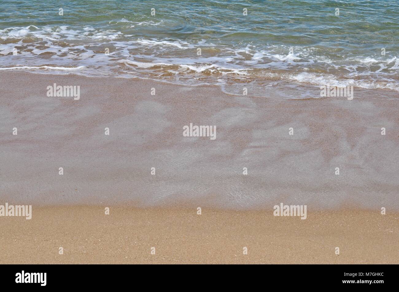 Small waves breaking at the shoreline with large area of wet sand. Stock Photo