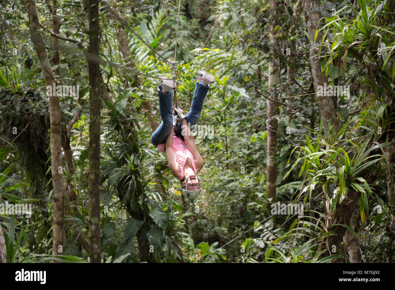 A woman (MR) flips upside down on a zipline ride through the jungle