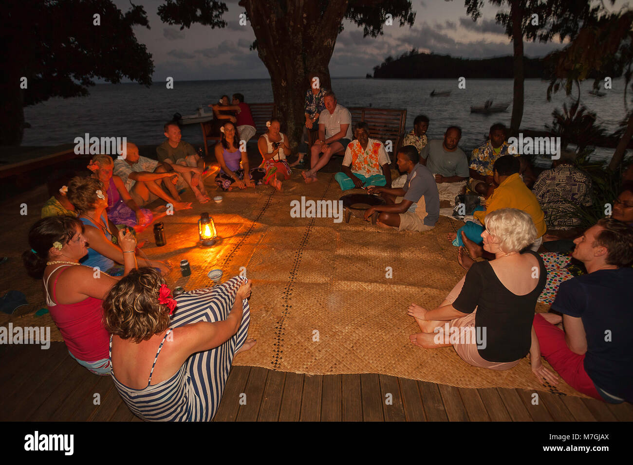 A group of guests seated in a circle on woven mats at the Matava Resort on the island of Kadavu, enjoying Kava, Fiji. Stock Photo