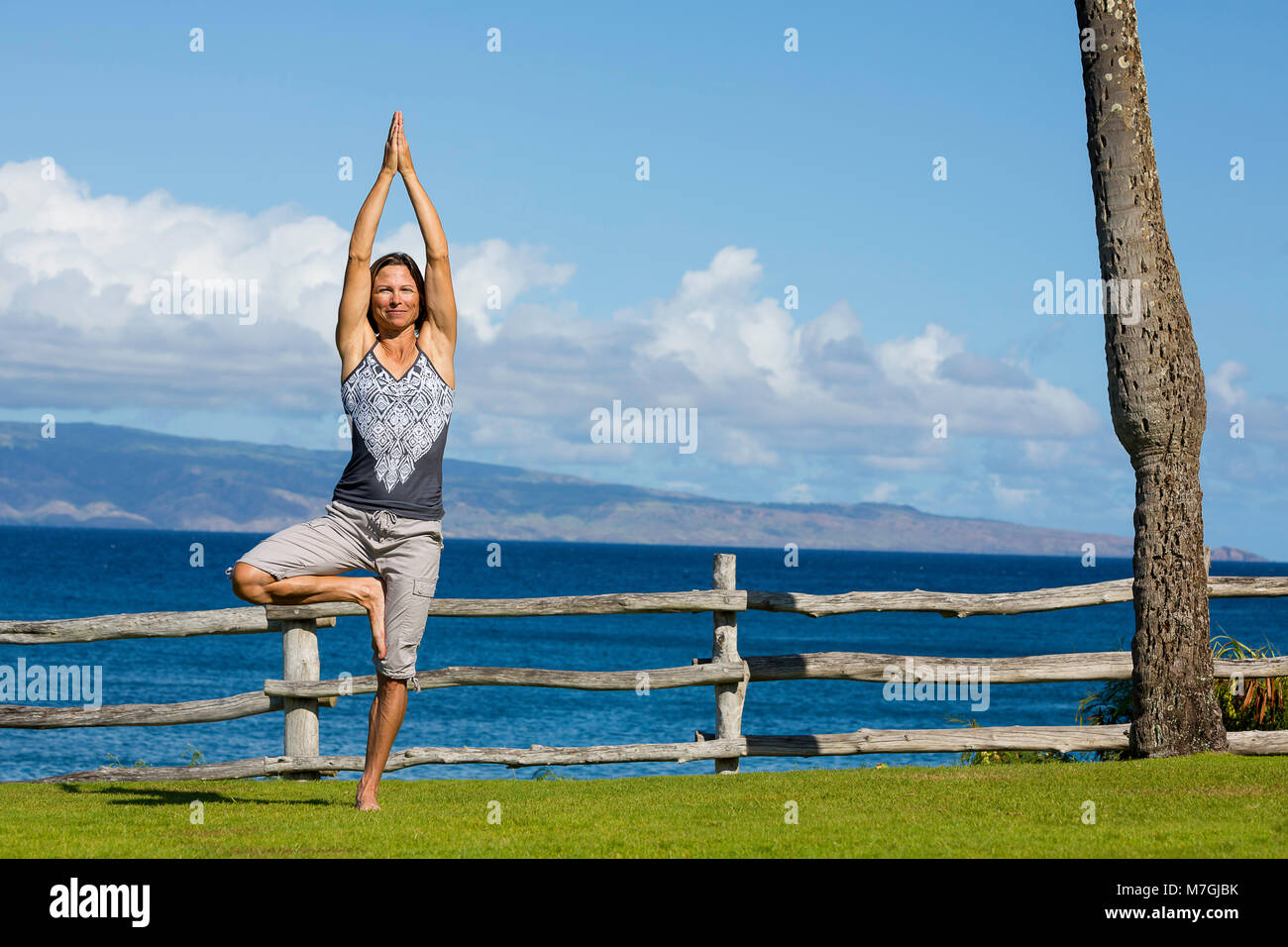 A woman (MR) in front of the ocean in a yoga position, Kapalua Bay, Maui, Hawaii, USA. Stock Photo