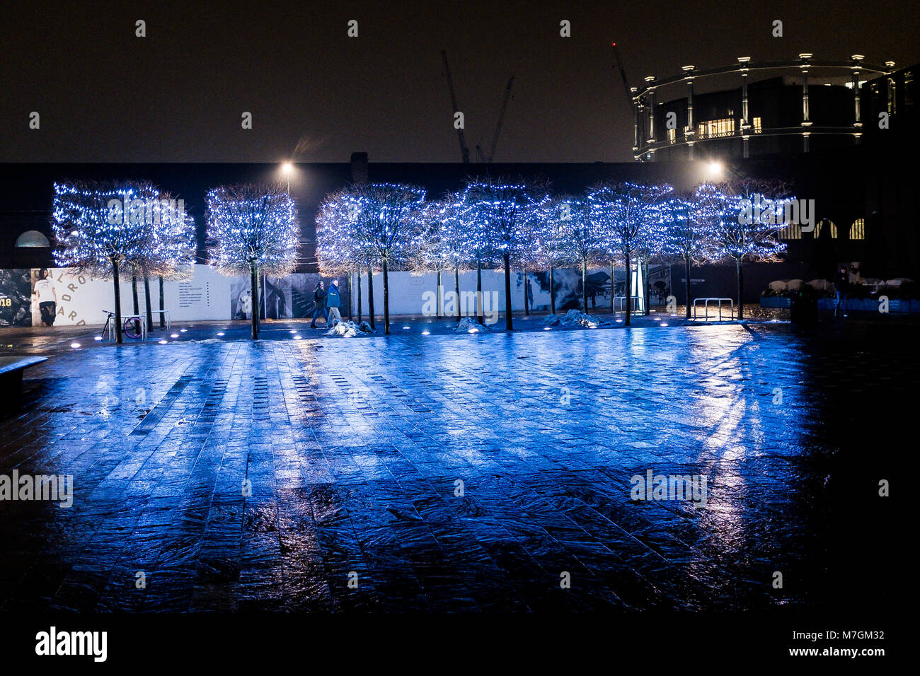 Illuminated trees at night in Granary Square in London’s Kings Cross with Gasholder Park in the background Stock Photo