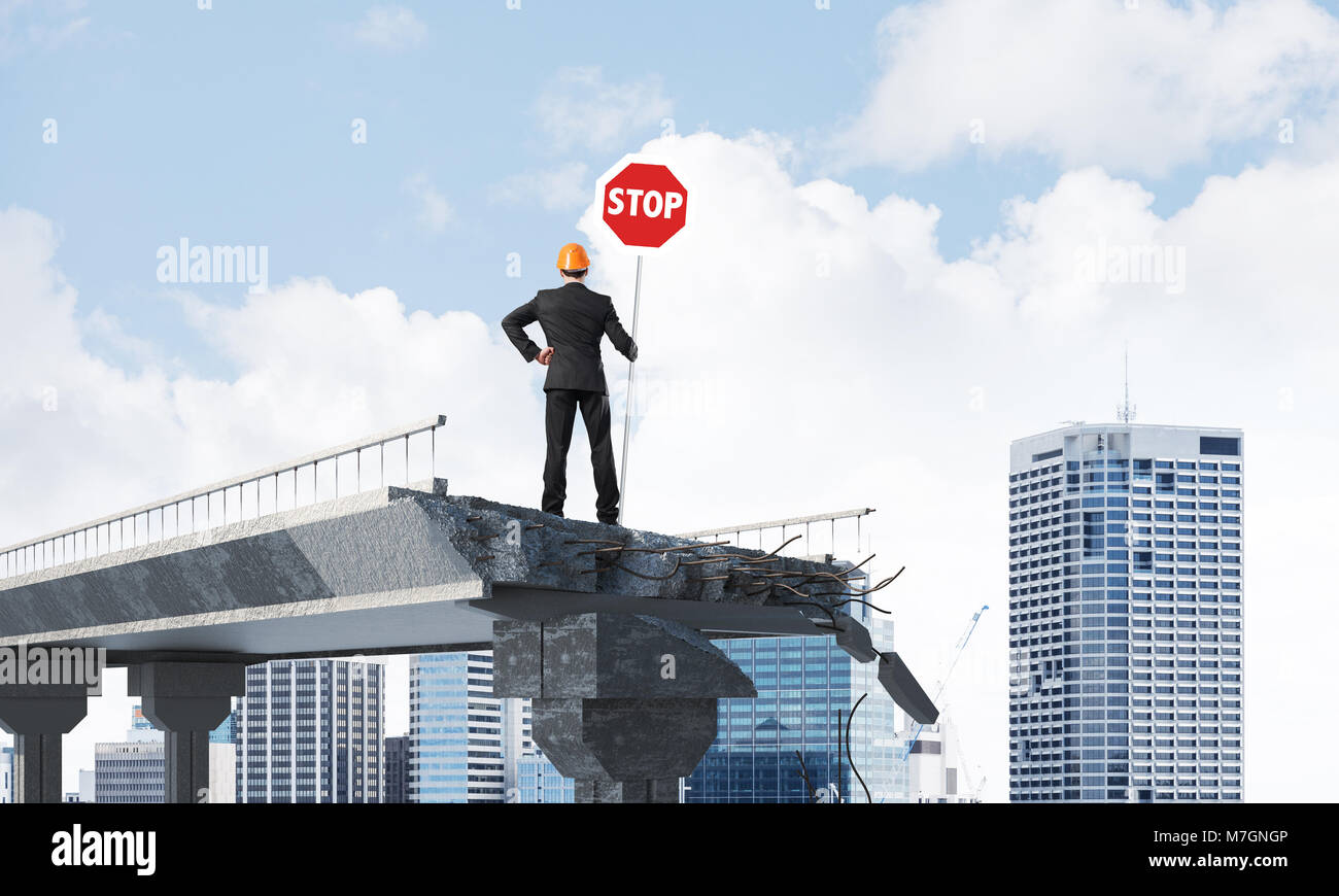 Rear view of engineer in helmet holding stop sign while standing on ...