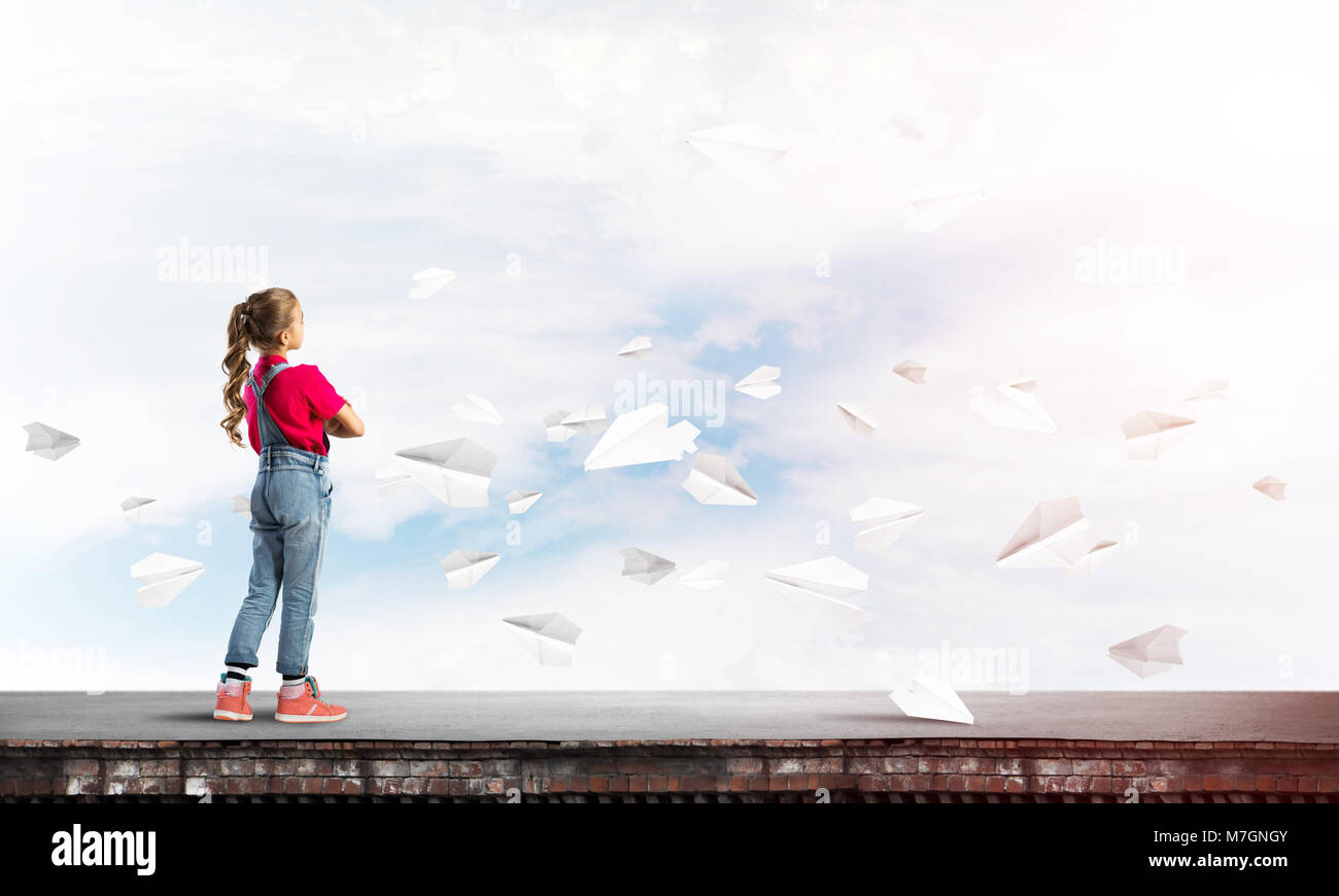 Cute kid girl standing on building roof and paper planes flying around ...