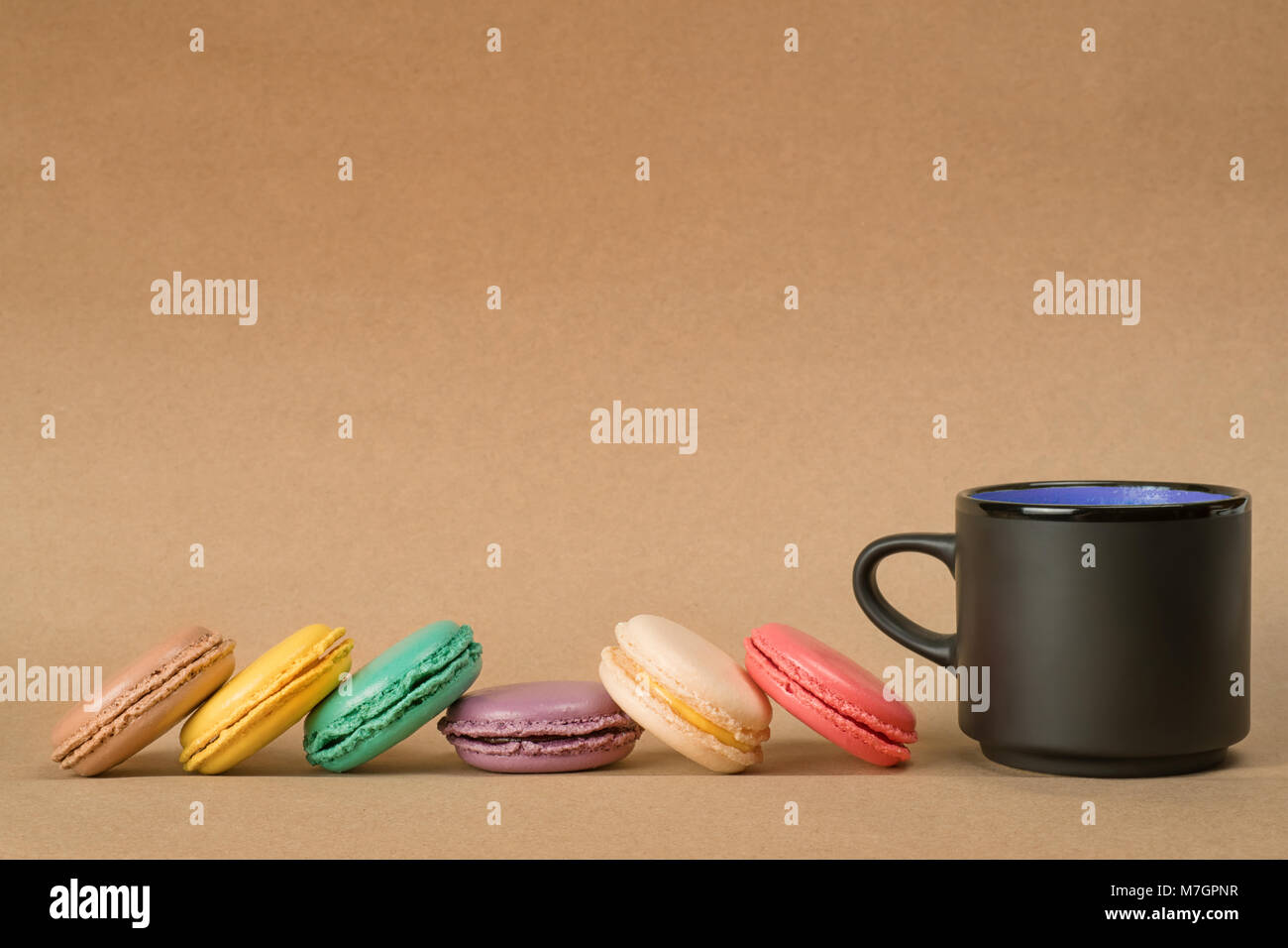Colored macaroons row and black coffee cup on brown craft paper background. Side view with copy space Stock Photo