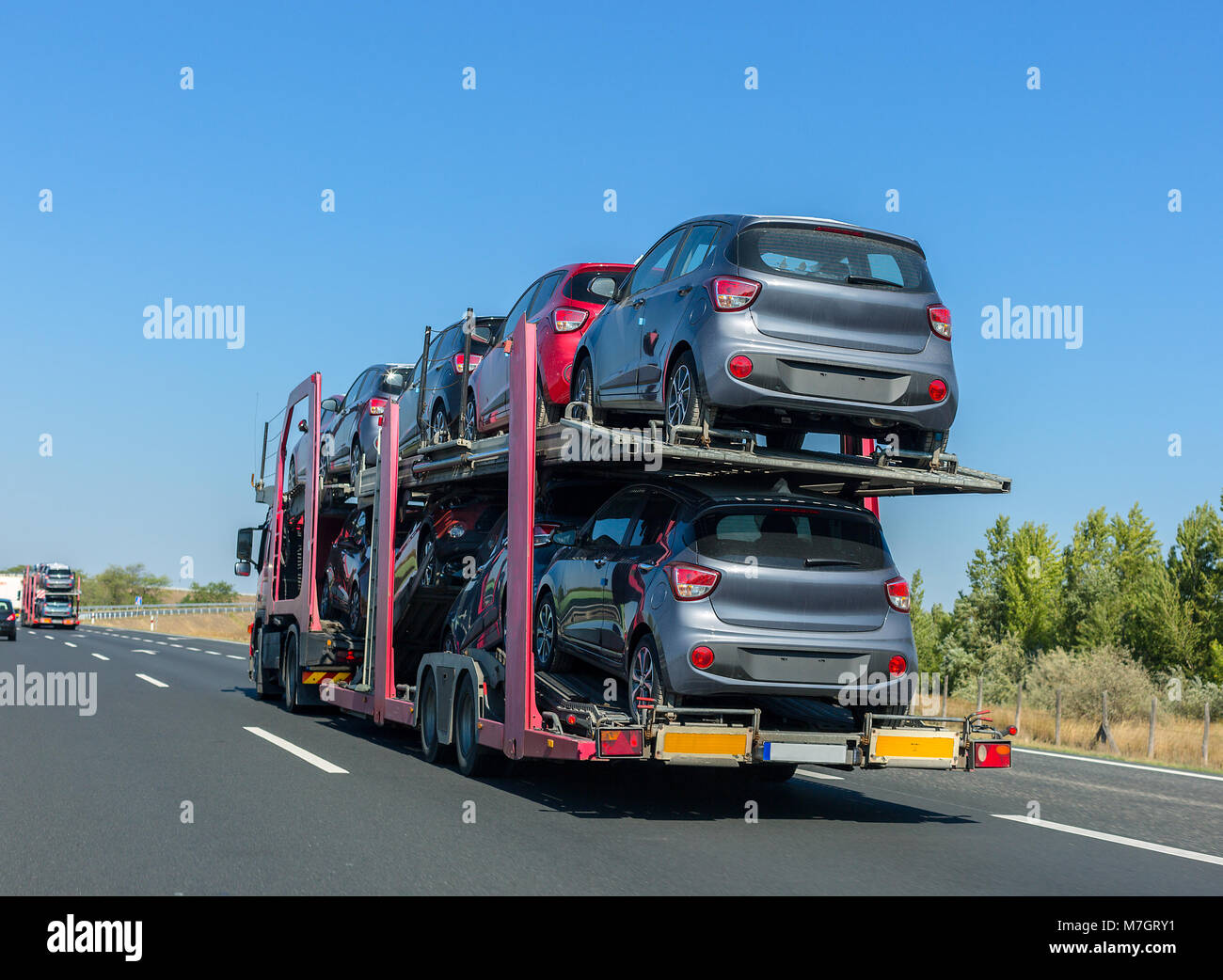 Big car carrier trailer with cars on bunk platform. Car transport truck on the highway Stock Photo