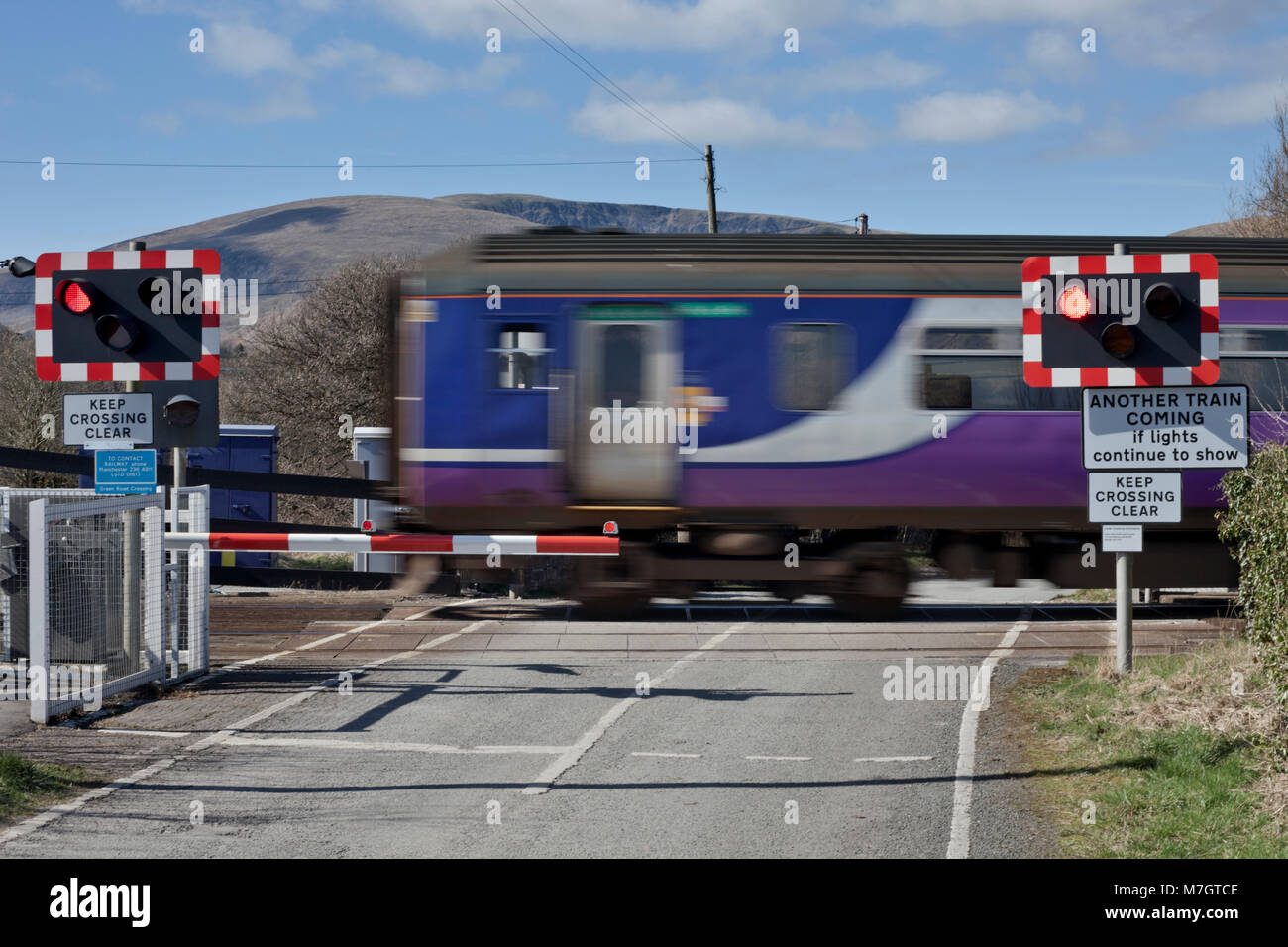 An Northern rail sprinter train crosses the automatic half barrier level crossing at Green road, Millom, Cumbria Stock Photo