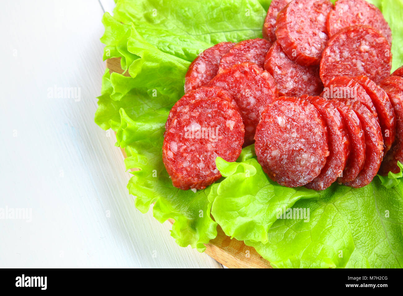 Smoked sausage, salami chopped in slices on a salad on a wooden circular cutting board on a white table Stock Photo