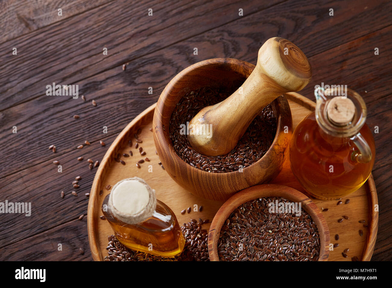 Flax seeds in bowl, wooden mortar and pestle and flaxseed oil in glass bottle on wooden tray