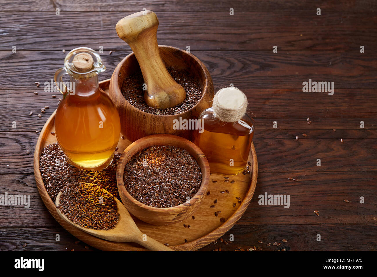 Flax seeds in bowl, wooden mortar and pestle and flaxseed oil in glass bottle on wooden tray