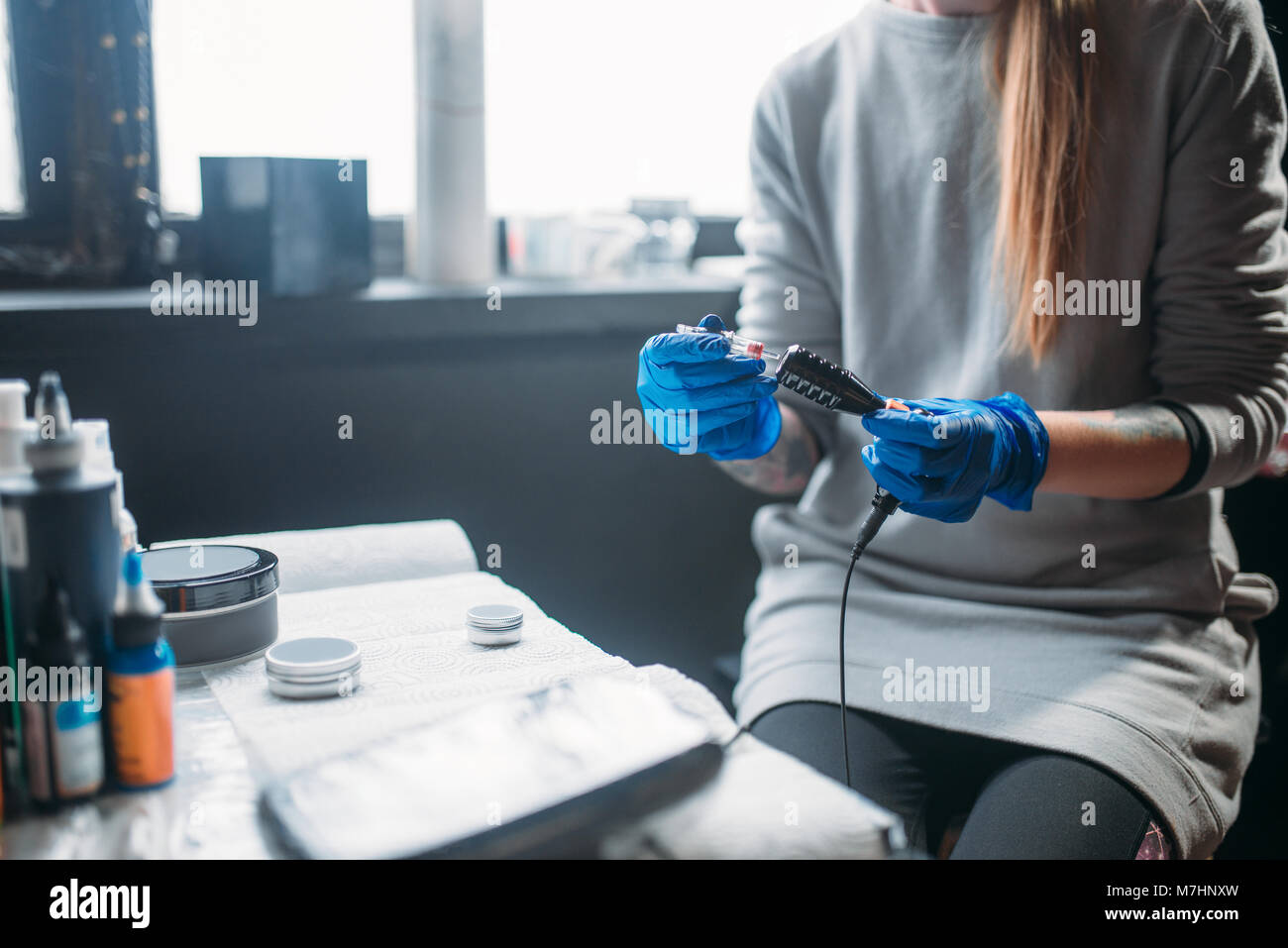 Female tattooer in blue sterile gloves prepares tattoo machine
