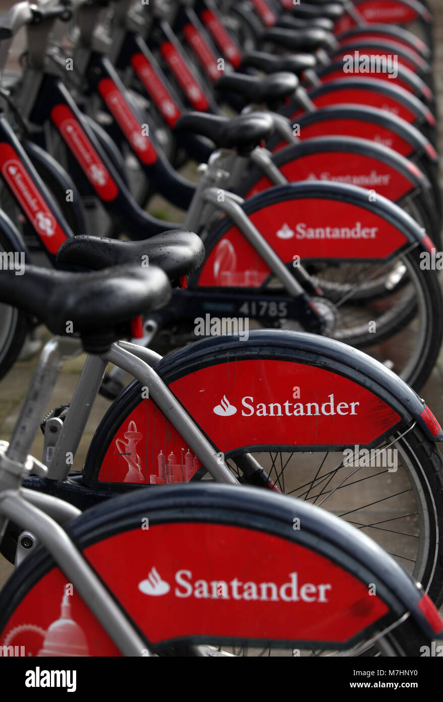 Santander branded bicycles for hire are secured in racks on the north side of the River Thames, in Westminster, London on March 11, 2018. Stock Photo