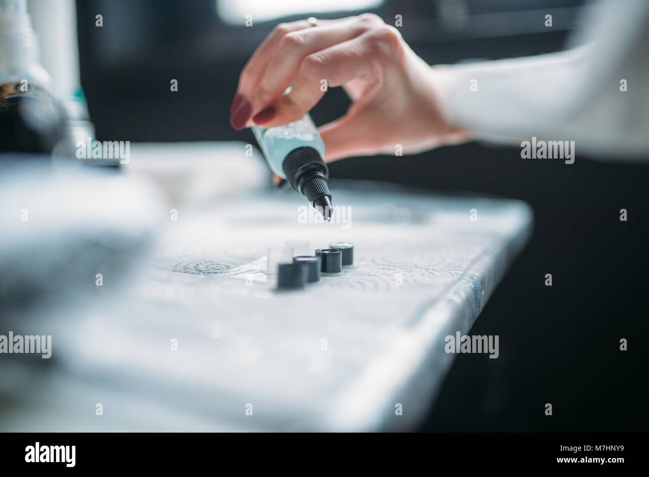 Female tattooist hands in blue sterile gloves holds tattoo machine