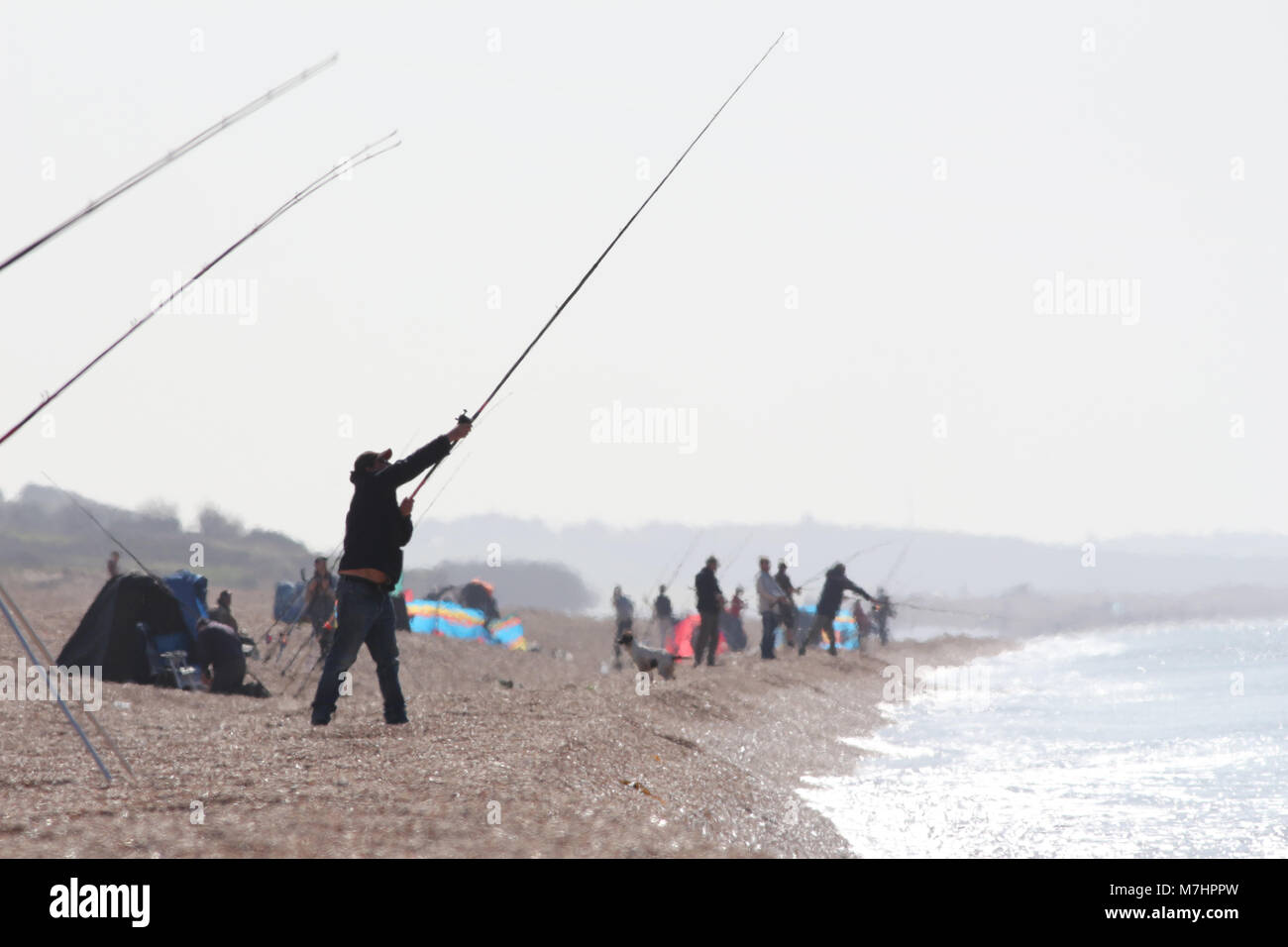 Anglers in a heat haze on a scorching day on Chesil beach UK, mostly fishing for mackerel Stock Photo